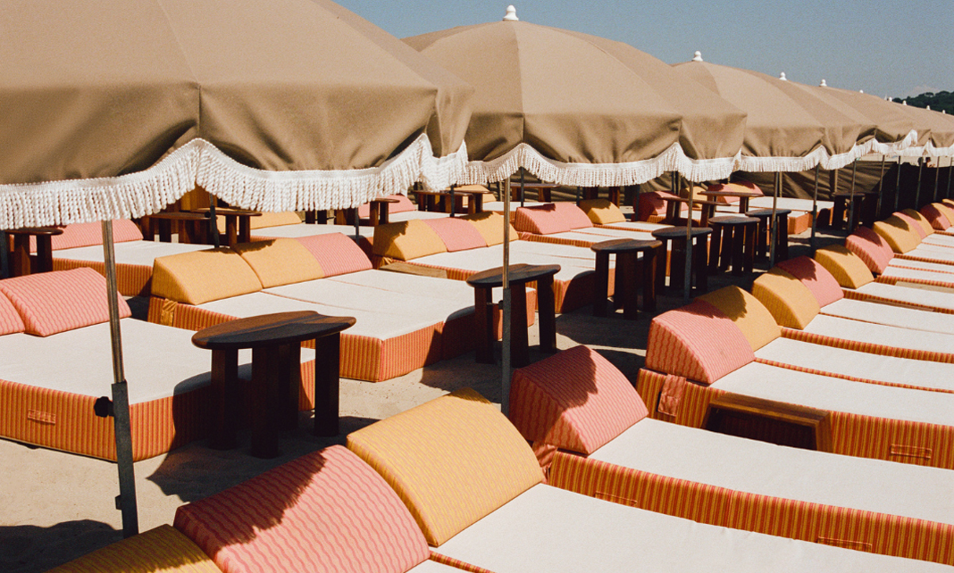 Transats et parasols de la plage priv&eacute;e Indie Beach Ramatuelle avec yachts et &icirc;les en fond